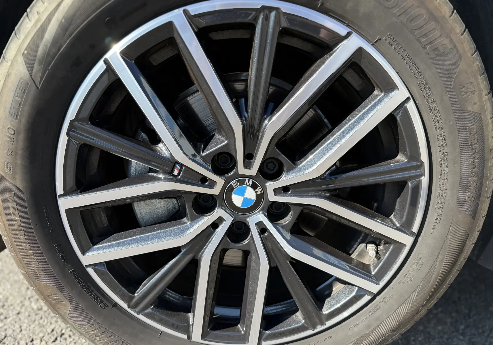 Gros plan sur la jante alliage noire et argentée avec logo BMW, montée sur pneu Bridgestone du BMW X1 blanc mineral.