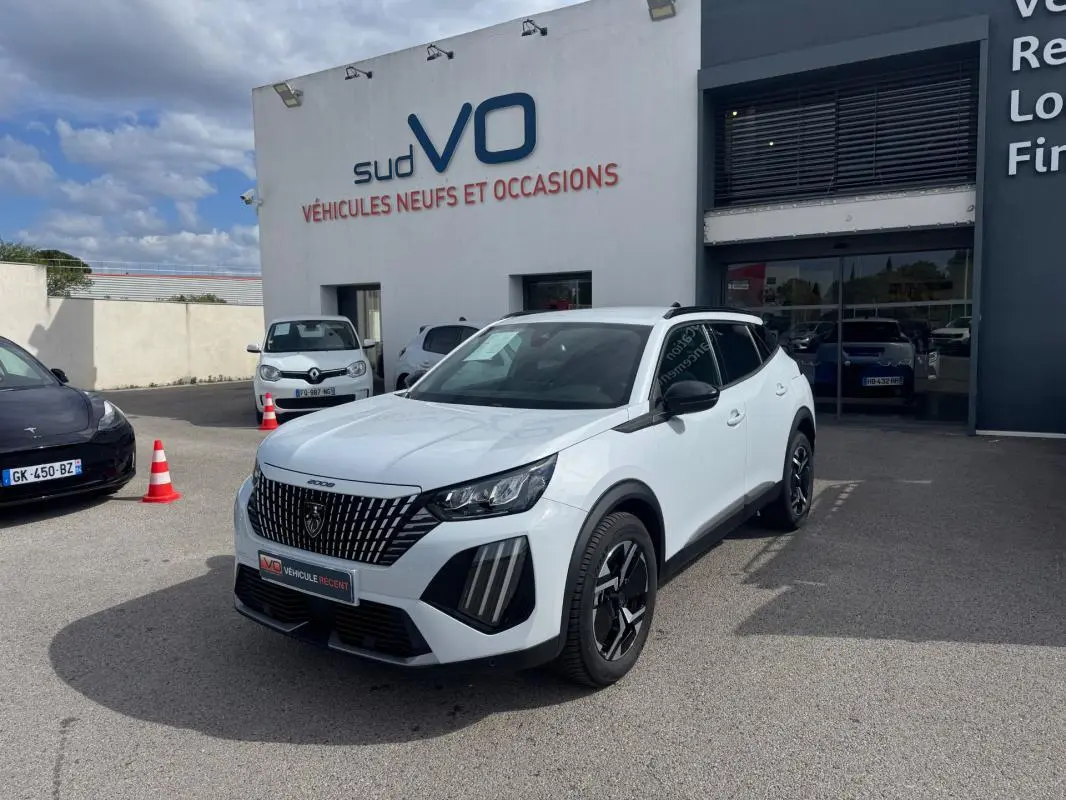 Peugeot 2008 blanc en 3/4 avant droit, avec barres de toit noires et jantes alliage 17 pouces visibles.