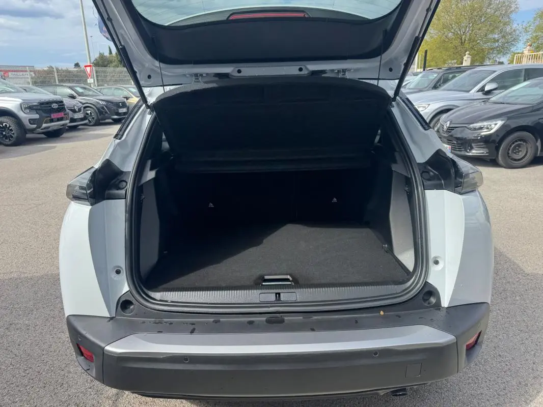 Coffre ouvert vu de l'arrière d'un Peugeot 2008 blanc 2024, avec pare-chocs noir et feux arrière sombres.