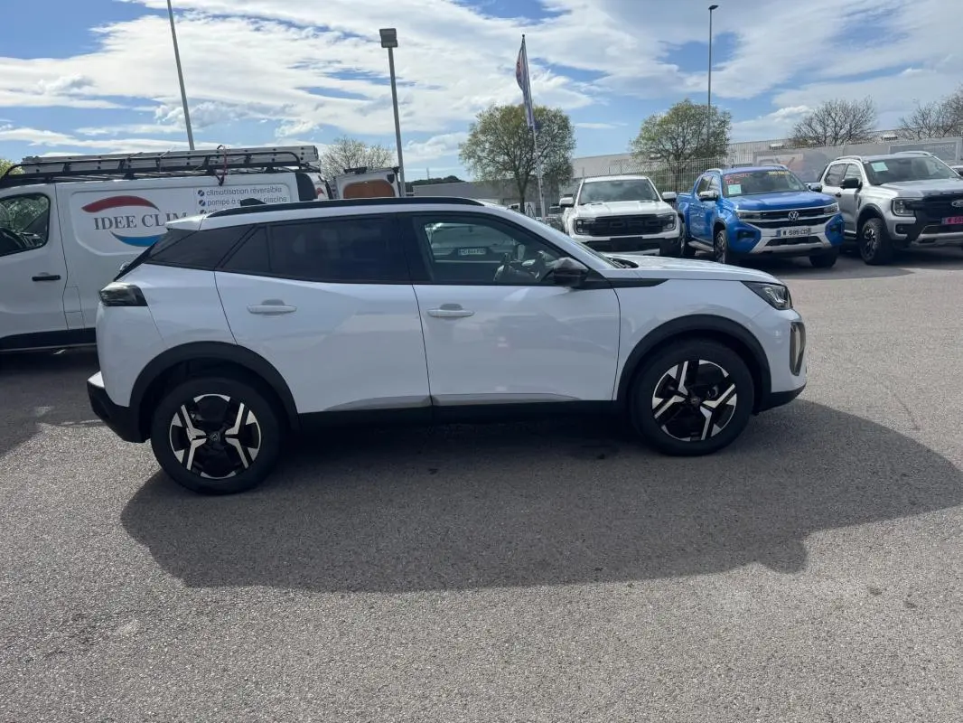 Peugeot 2008 blanc vue de profil côté gauche, avec barres de toit et jantes alliage 17 pouces visibles.
