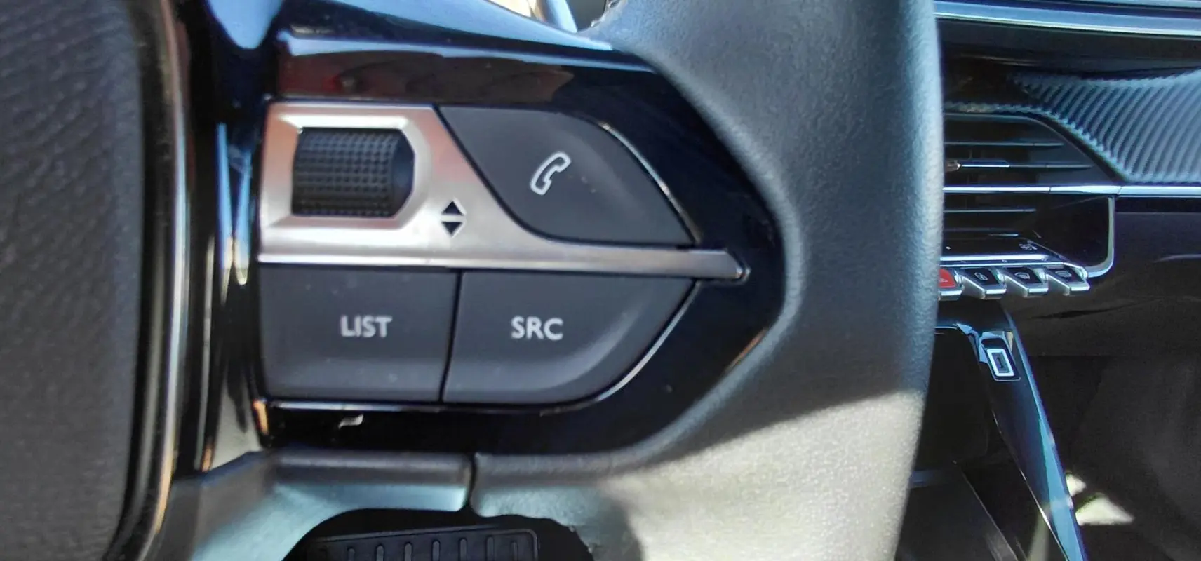 Gros plan sur les commandes au volant du Peugeot 2008 Hybrid 136 e-DCS6 Style, intérieur noir avec détails argentés.