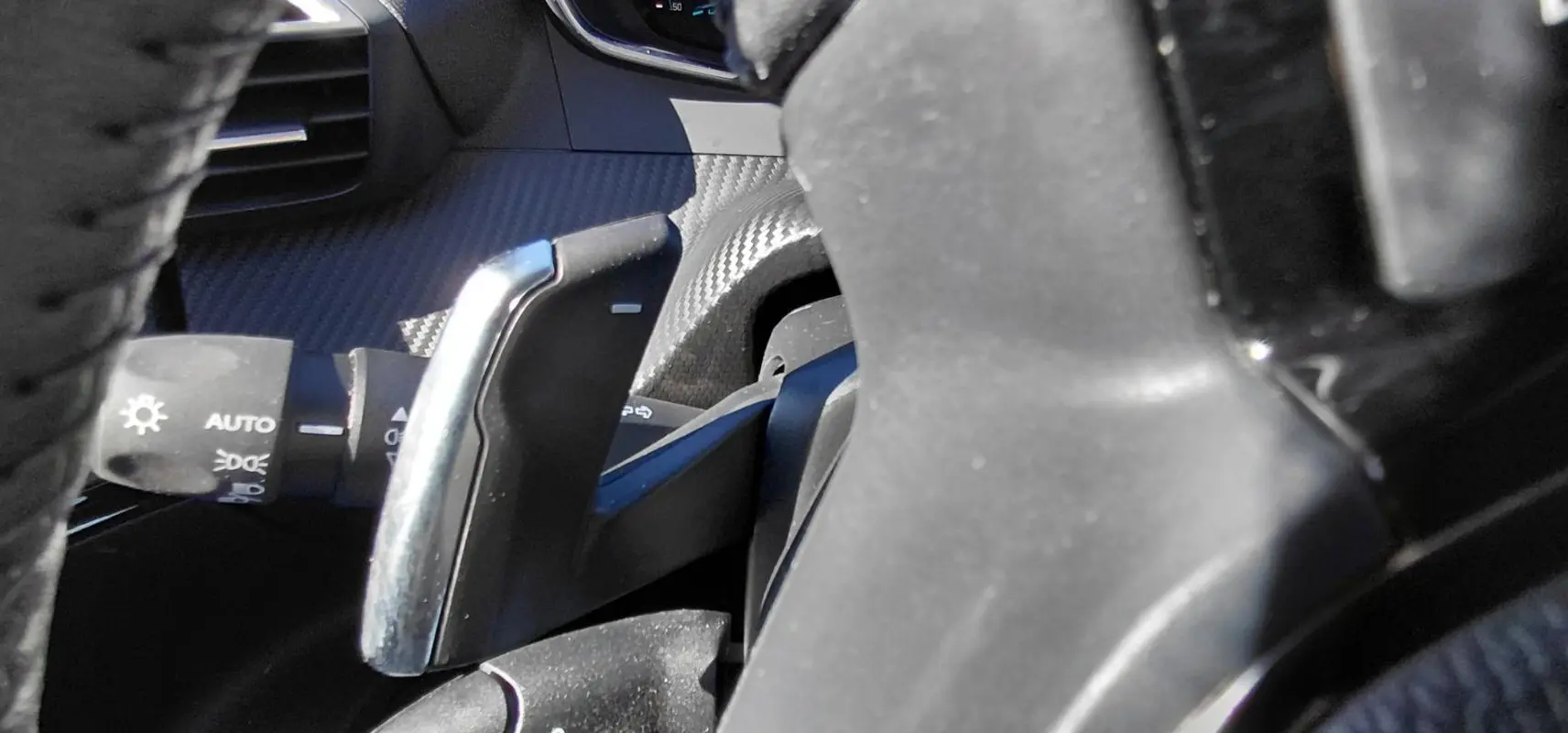 Gros plan sur la palette de changement de vitesse derrière le volant d’un Peugeot 2008 Hybrid bleu, intérieur noir.