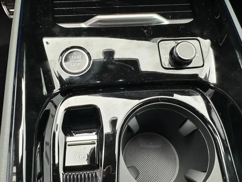 Gros plan sur la console centrale noire brillante de l'Audi Q3 2026 avec bouton start/stop et molette de commande multimédia.