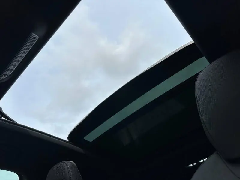 Vue intérieure du toit ouvrant panoramique du SUV Audi Q3 noir Mythique métallisé, avec ciel nuageux visible à travers le verre.