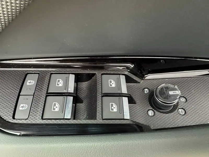 Gros plan sur les commandes des vitres et des rétroviseurs côté conducteur d’un Audi Q3 noir Mythique métallisé.