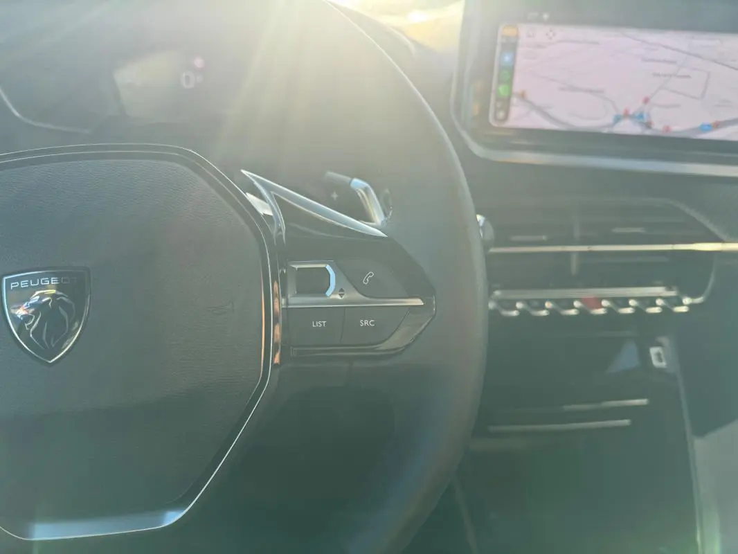Vue intérieure rapprochée du volant noir du Peugeot 2008 Hybrid 136 Allure avec écran tactile et commandes au volant.