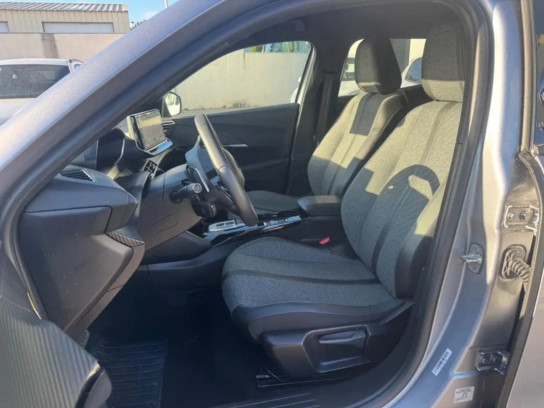 Intérieur avant droit du Peugeot 2008 Hybrid gris 2024, sièges tissu gris et tableau de bord moderne avec écran tactile.
