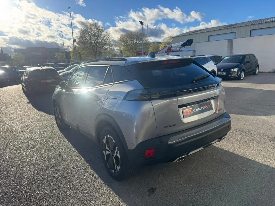 Vue 3/4 arrière droite d’un Peugeot 2008 Hybrid gris avec barres de toit et jantes alliage 17 pouces, stationné en extérieur.