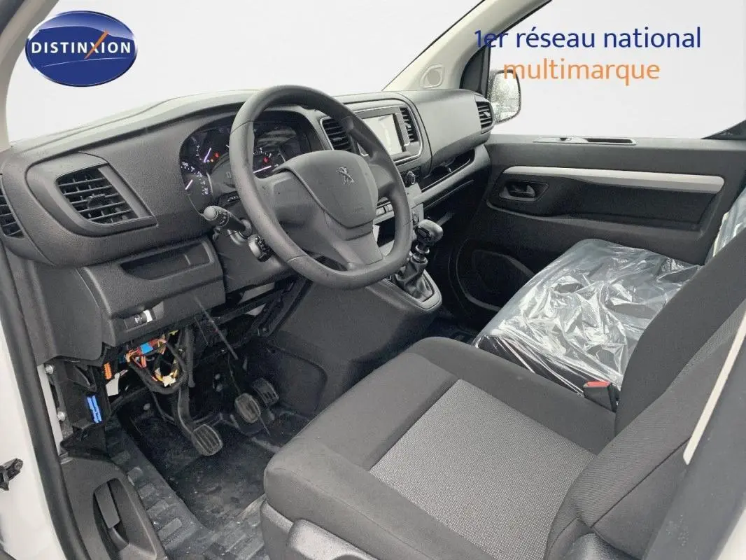 Vue intérieure côté conducteur du Peugeot Expert Fourgon 2023, tableau de bord noir avec volant et siège plastique.