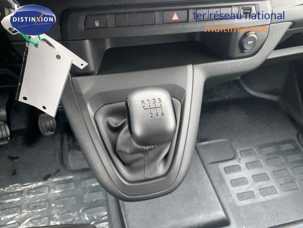 Gros plan sur le levier de vitesses manuel gris du Peugeot Expert Fourgon blanc, avec tableau de bord et pédales visibles.