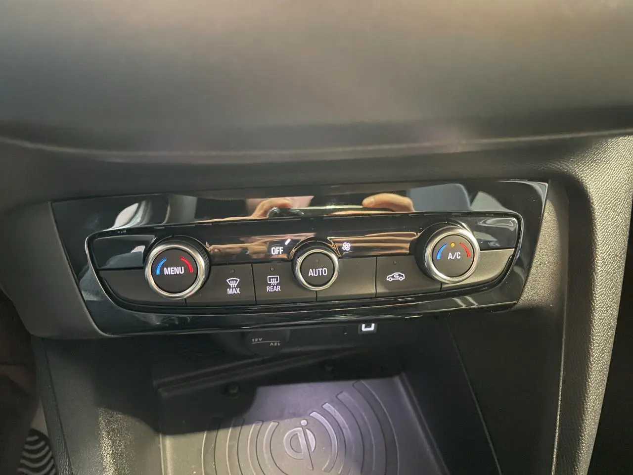 Détail de la console centrale noire avec commandes de climatisation et chargeur smartphone à induction dans Opel Corsa blanche.