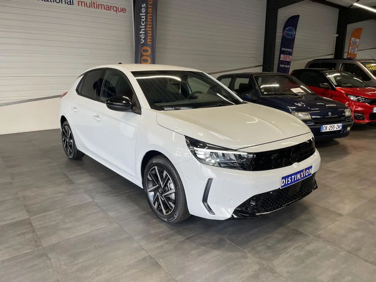 Opel Corsa blanche vue 3/4 avant droit en intérieur, avec calandre noire et jantes alliage diamantées.