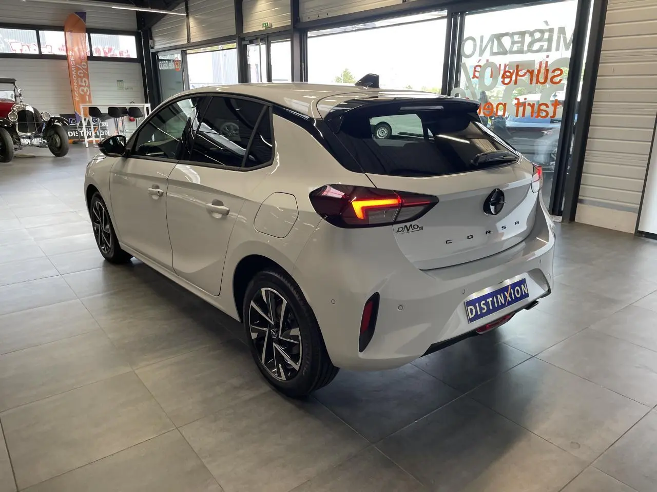 Vue 3/4 arrière droite d'une Opel Corsa blanche avec feux LED allumés et jantes alliage diamantées en showroom.