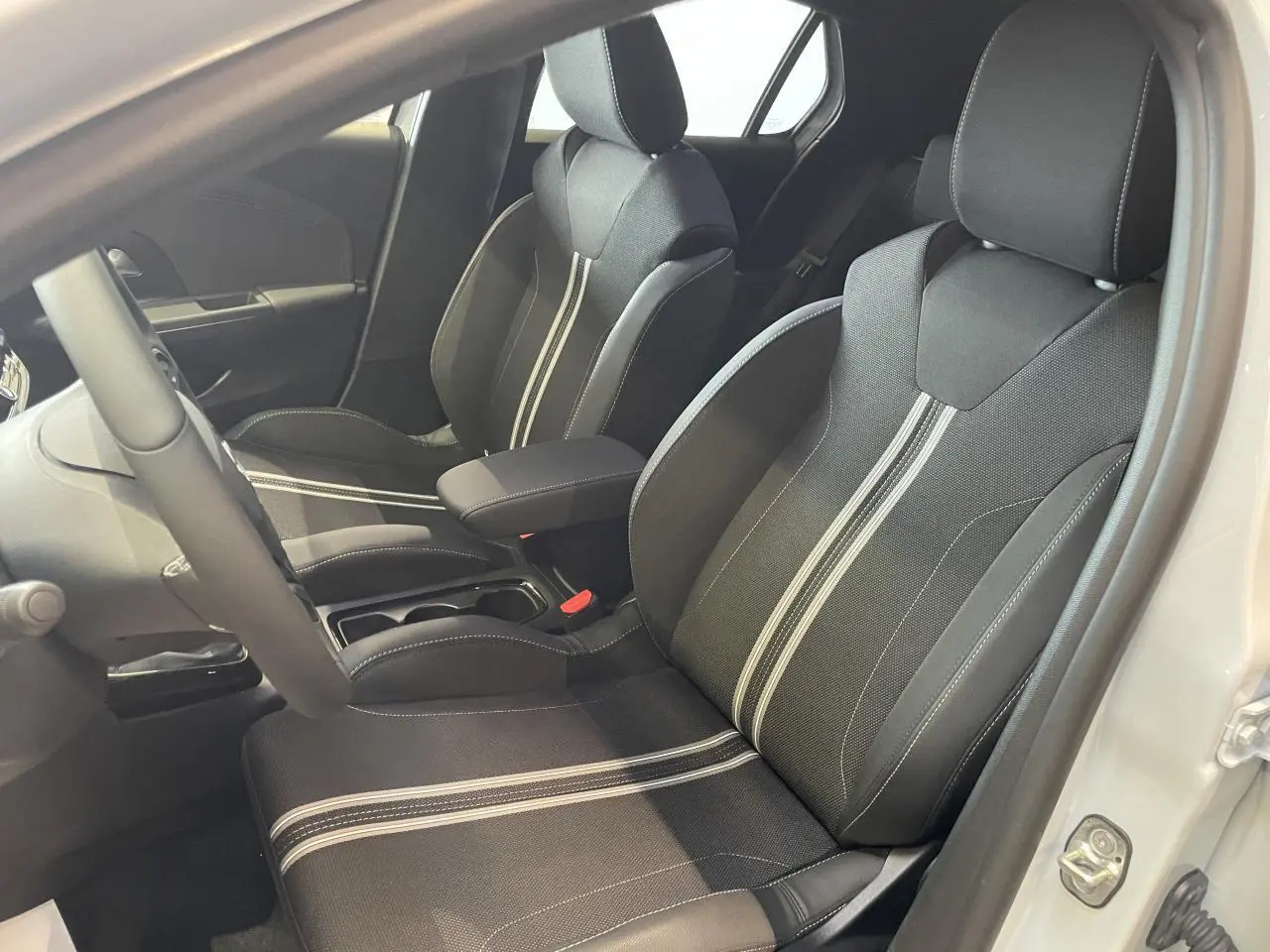 Vue intérieure côté conducteur de l'Opel Corsa blanc, sièges sport noirs avec bandes blanches centrales et accoudoir.