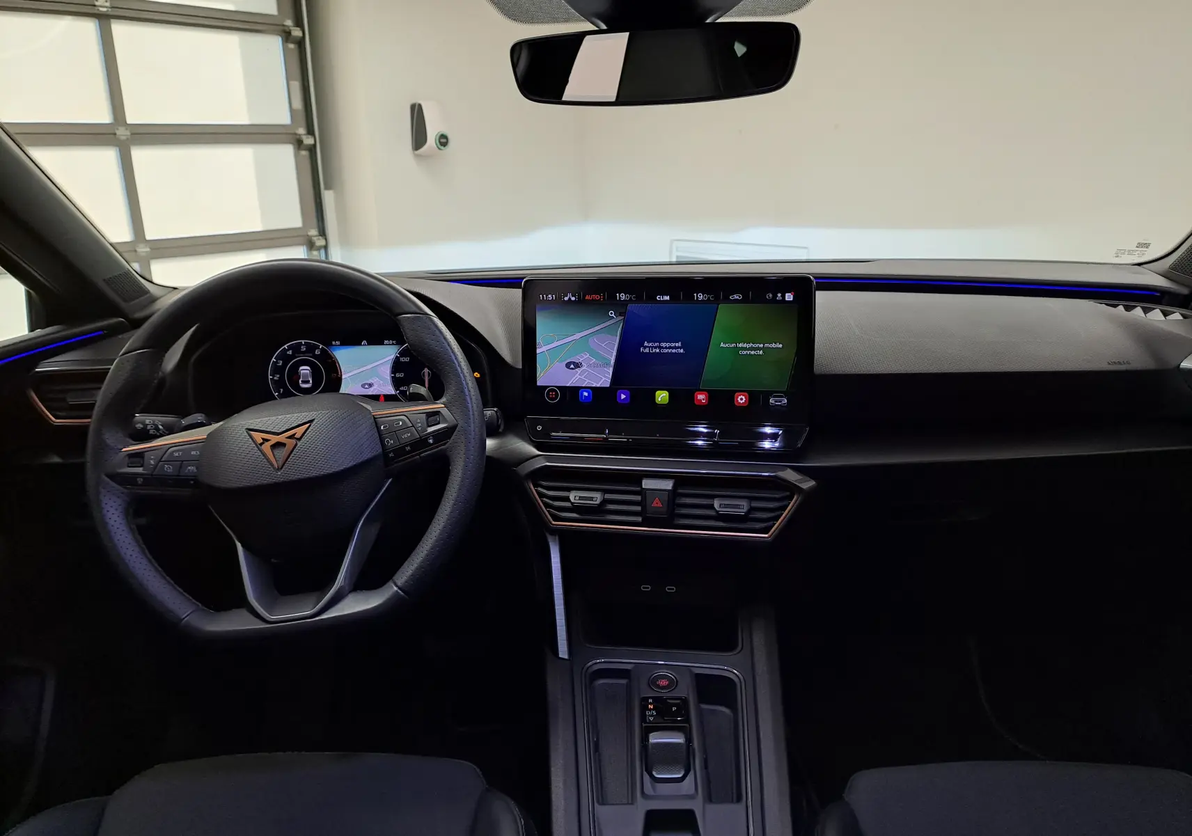 Vue intérieure avant du CUPRA Leon 2024 avec tableau de bord noir, écran tactile central et volant multifonction.