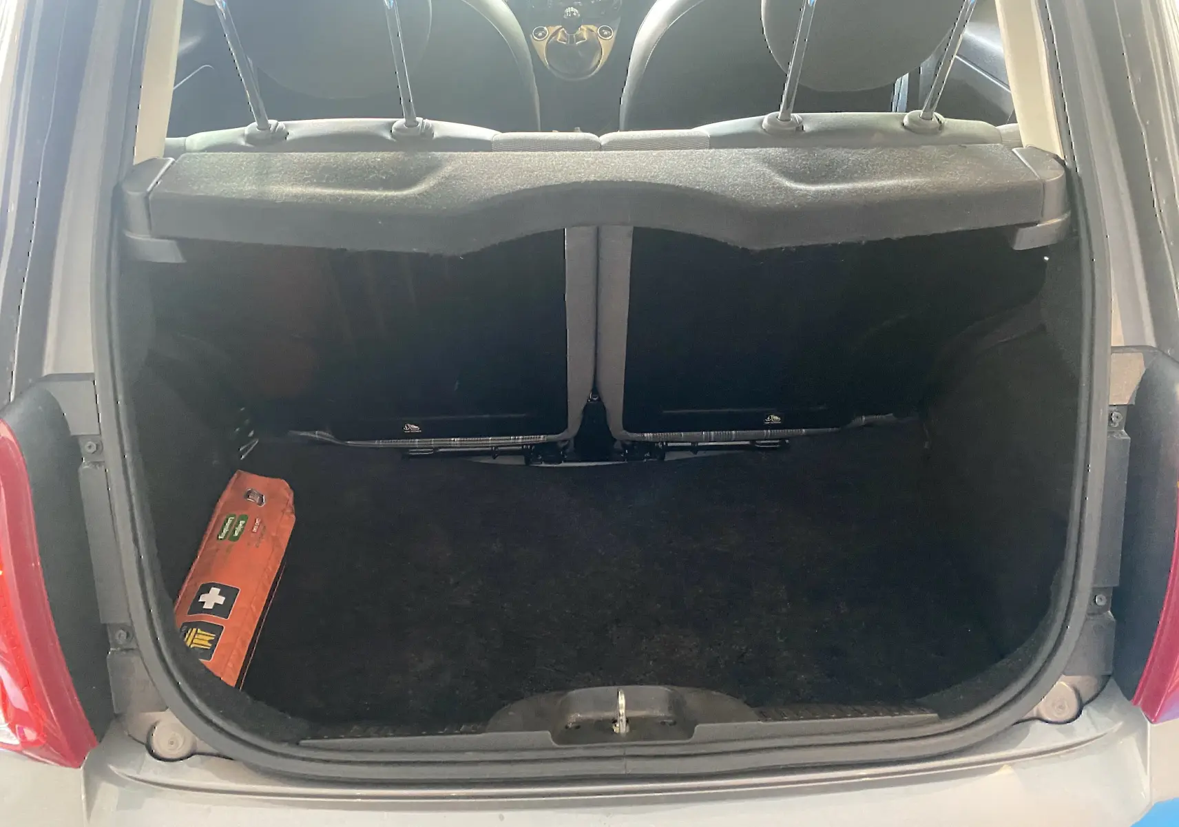 Vue du coffre arrière ouvert d'une Fiat 500 gris foncé, avec un kit de secours orange visible sur la gauche.