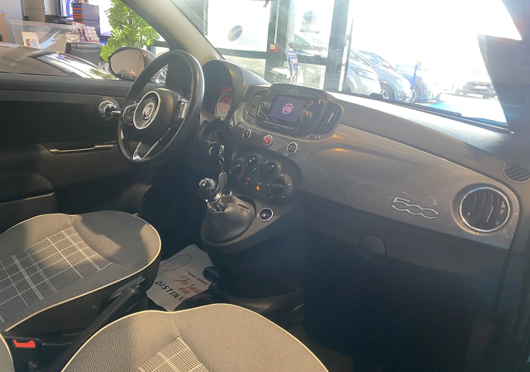 Vue intérieure côté conducteur de la Fiat 500 2019 gris foncé, avec tableau de bord brillant et volant multifonction.