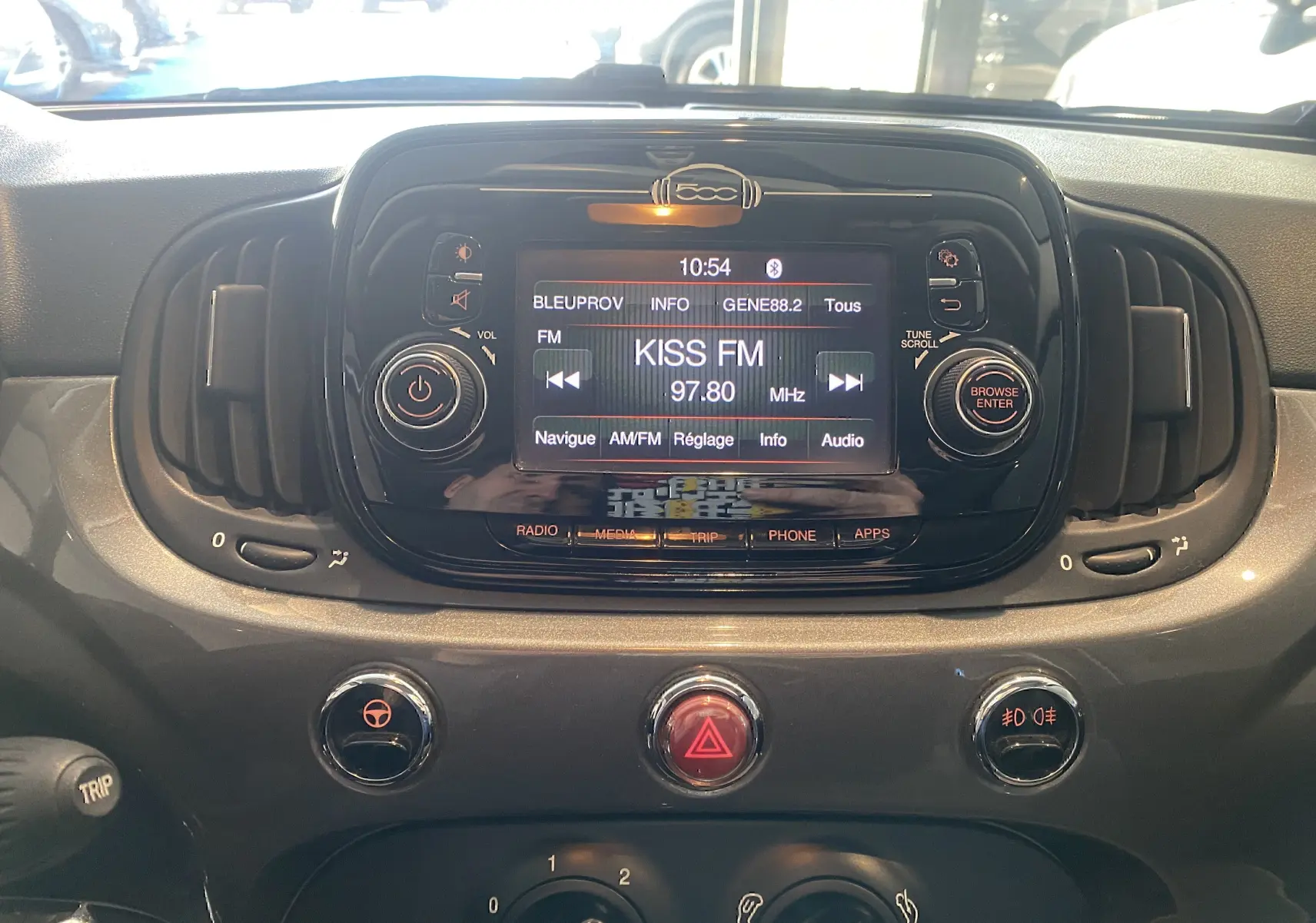 Vue rapprochée du tableau de bord noir de la Fiat 500 avec écran central affichant la radio Kiss FM.