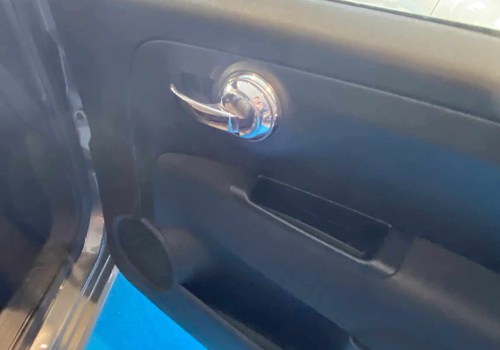 Gros plan sur la poignée intérieure chromée de la porte côté gauche d'une Fiat 500 gris foncé, finition Lounge.