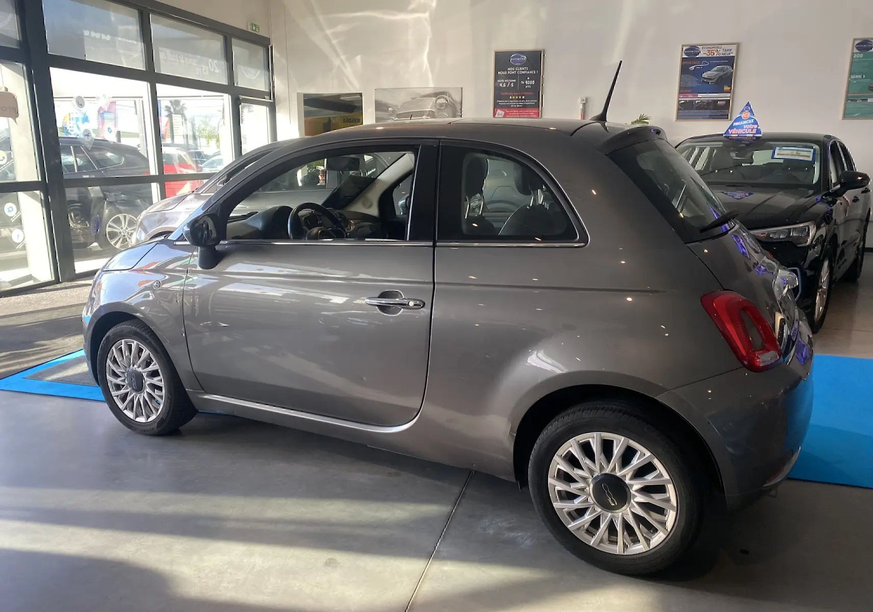 Vue de profil côté gauche d'une Fiat 500 gris foncé 2019 avec jantes alliage et toit noir en concession.