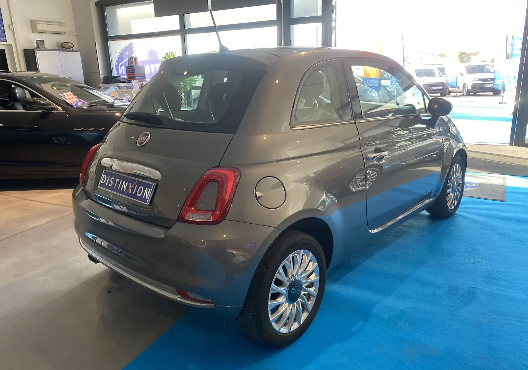 Vue 3/4 arrière droite d'une FIAT 500 gris foncé exposée en showroom avec jantes multibranches et intérieur noir.