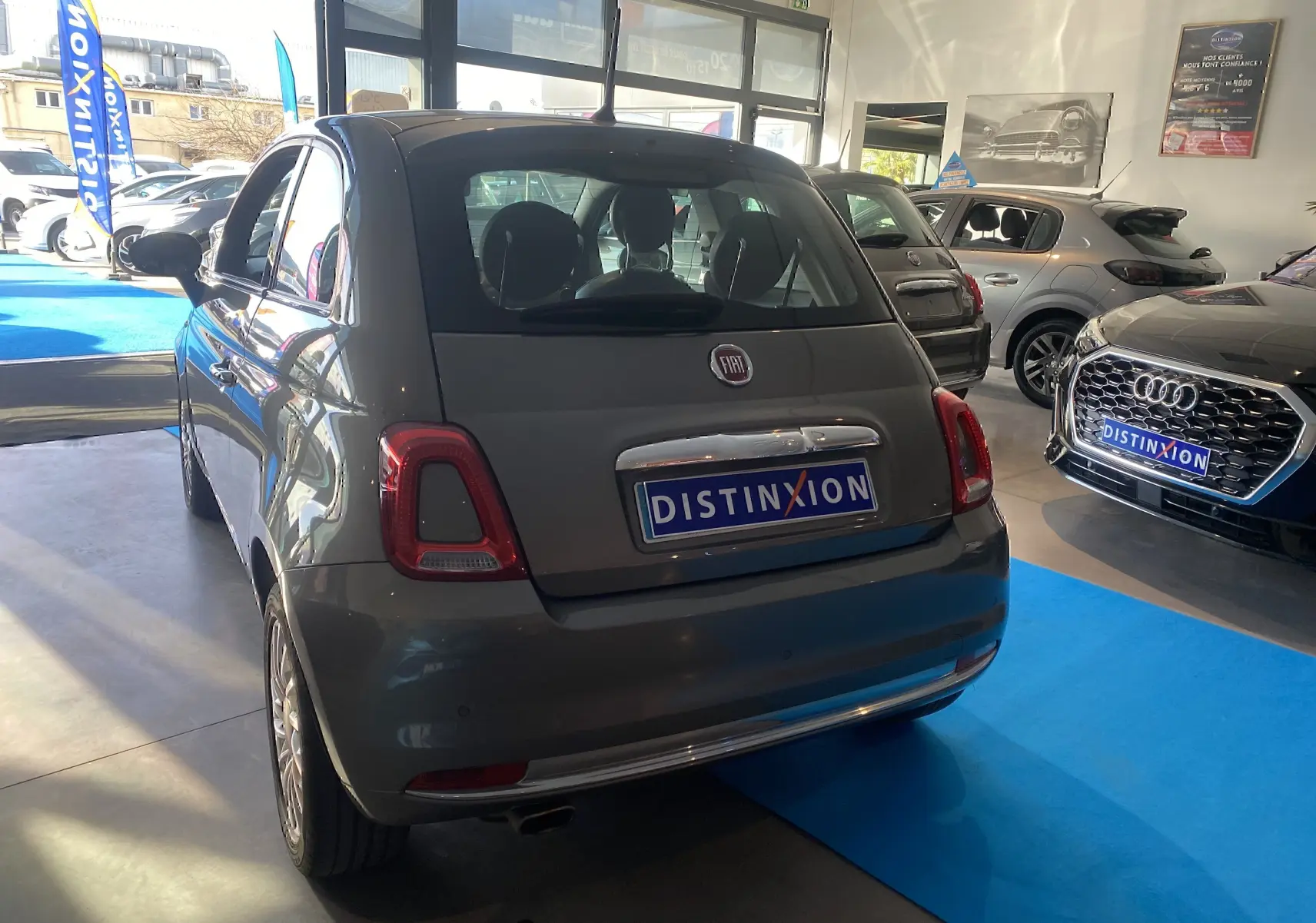 Vue 3/4 arrière droite d'une Fiat 500 gris foncé exposée en showroom avec plaque Distinxion visible.