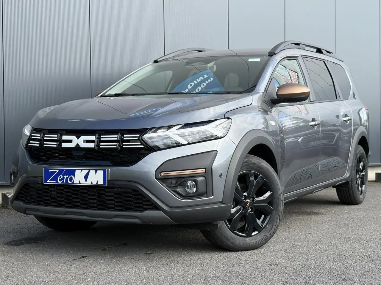 Dacia Jogger Gris Schiste en 3/4 avant droit, avec jantes noires et rétroviseur cuivré distinctif.