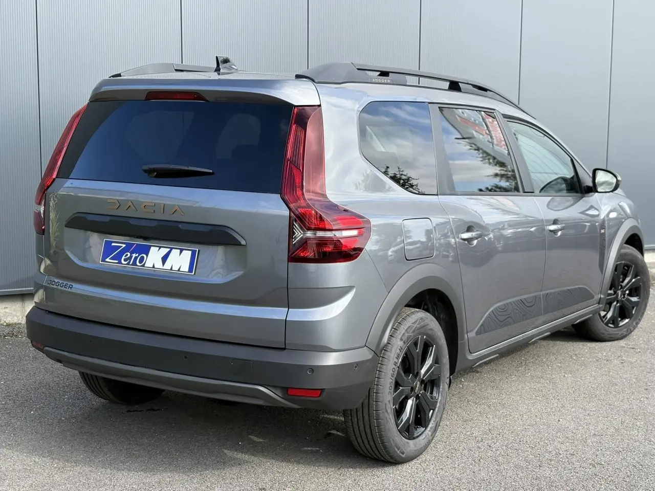 Vue 3/4 arrière droite du Dacia Jogger 2024 Gris Schiste avec jantes noires et barres de toit modulaires.