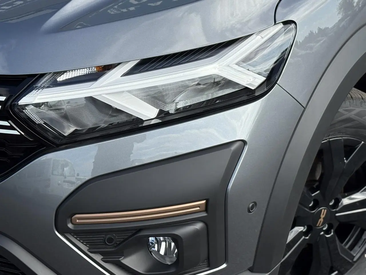 Gros plan sur l'avant droit gris schiste du Dacia Jogger 2024, mettant en valeur le phare LED et la jante noire.