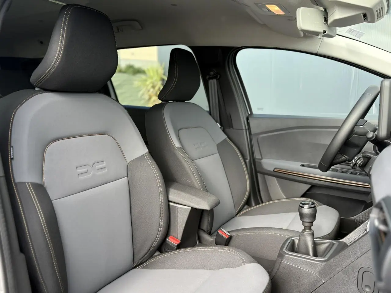 Intérieur du Dacia Jogger 2024 vu côté droit, sièges gris avec surpiqûres et accoudoir central, volant et levier de vitesses visibles.
