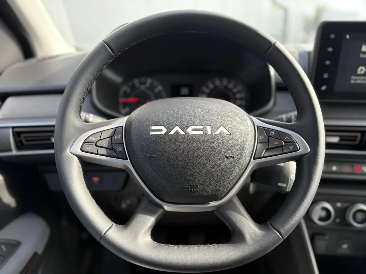 Volant en cuir noir avec commandes intégrées du Dacia Jogger 2024, tableau de bord et écran tactile en arrière-plan.