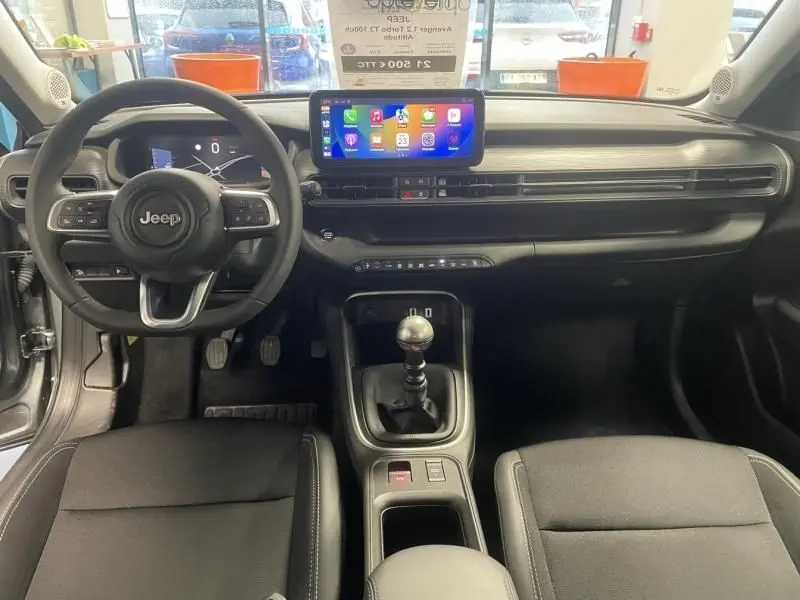 Vue intérieure avant du Jeep Avenger 2025 essence, tableau de bord noir avec écran tactile et levier de vitesse manuel.