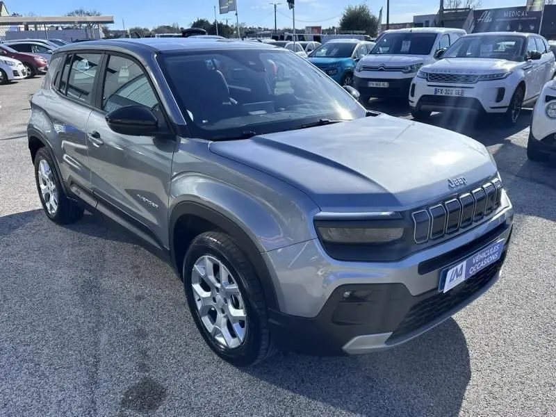 Jeep Avenger gris métallisé en 3/4 avant droit, avec calandre distinctive et jantes argentées visibles.