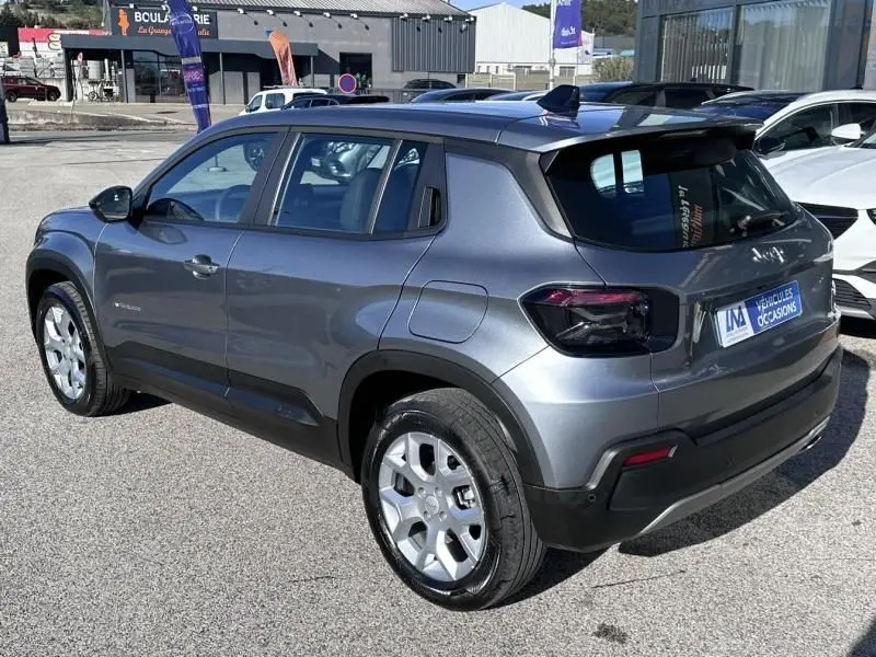 Jeep Avenger gris métallisé en 3/4 arrière droit, avec jantes argentées et toit noir contrasté visible en extérieur.