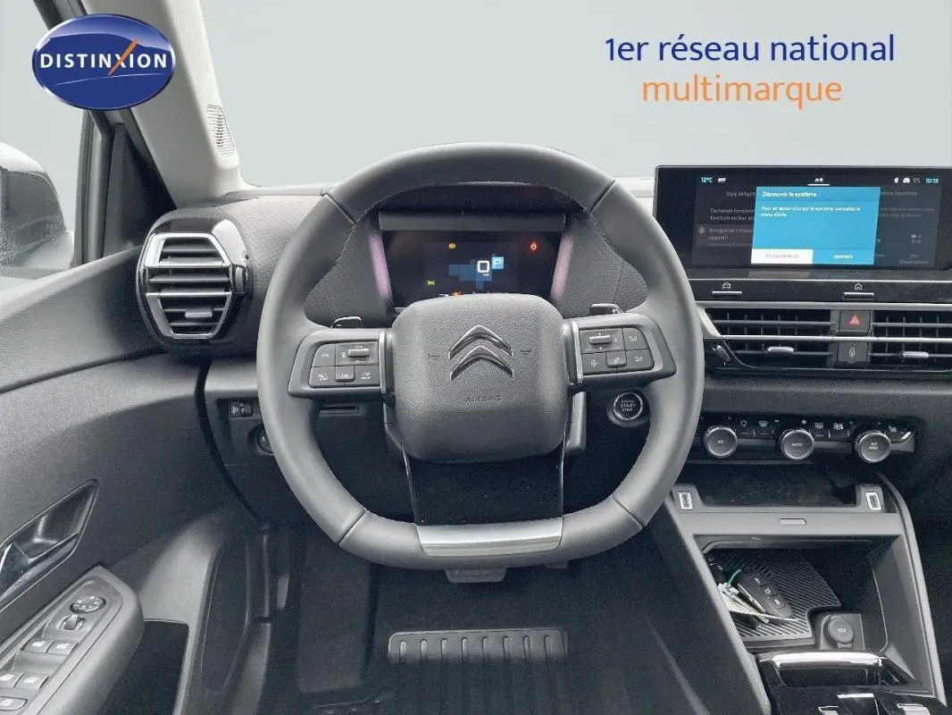 Vue intérieure centrée sur le volant cuir et tableau de bord numérique de la Citroën C4 blanche 2024.