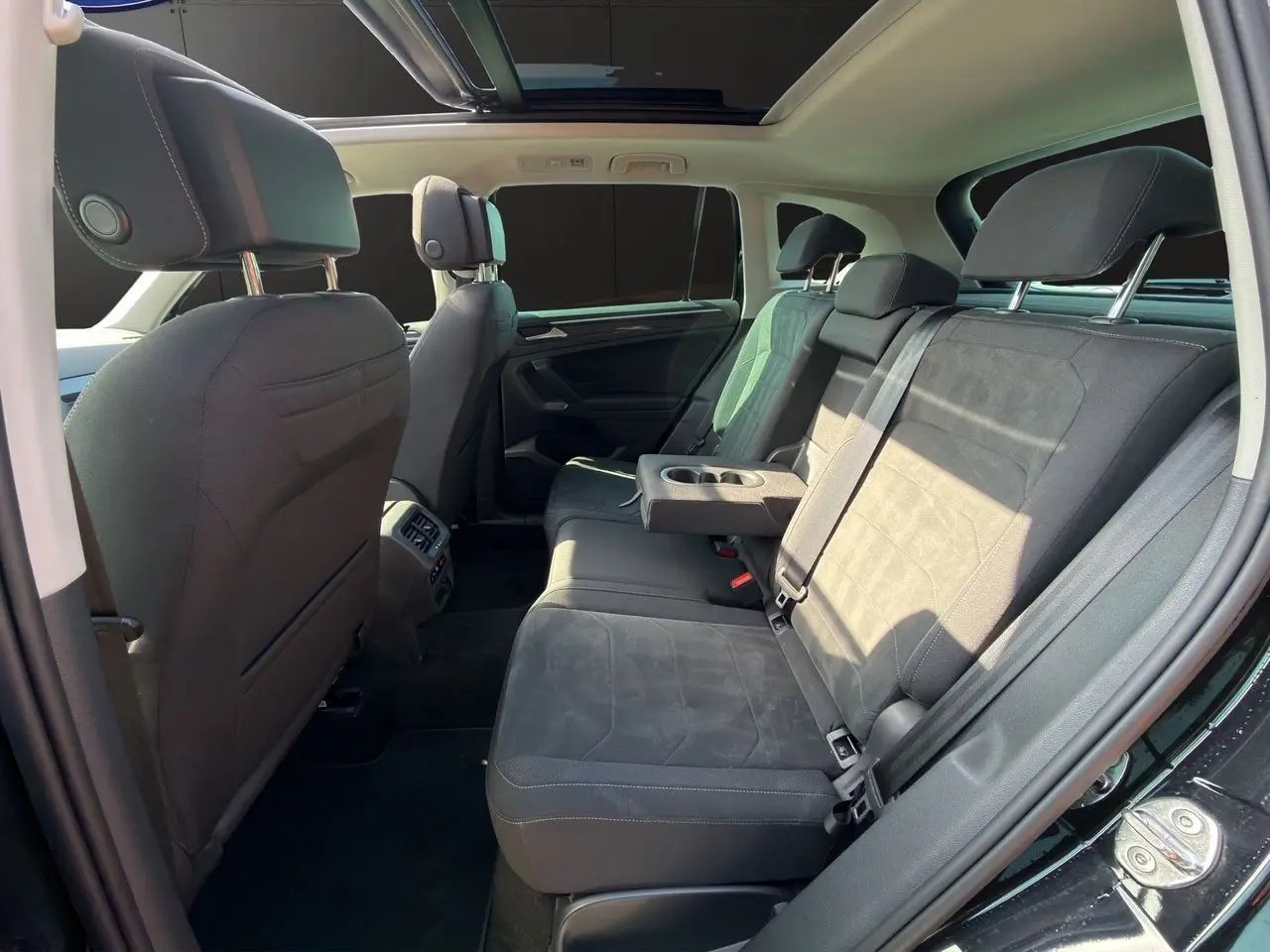Vue intérieure côté droit des sièges arrière noirs du Volkswagen Tiguan 2.0 TDI avec accoudoir central et toit panoramique.