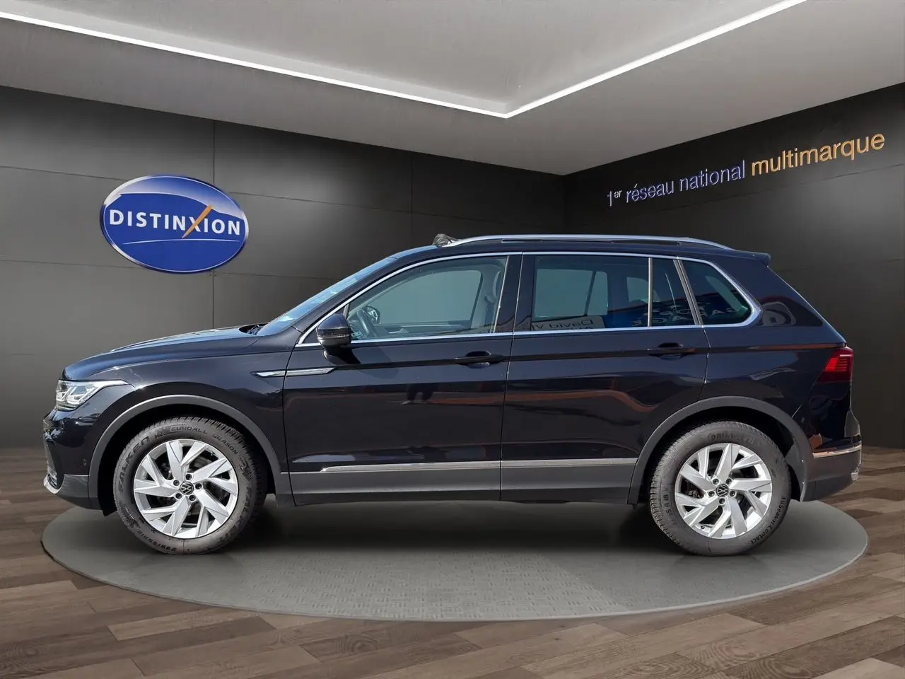 Vue de profil côté gauche d'un Volkswagen Tiguan noir intense avec jantes alu 18 pouces dans un showroom.