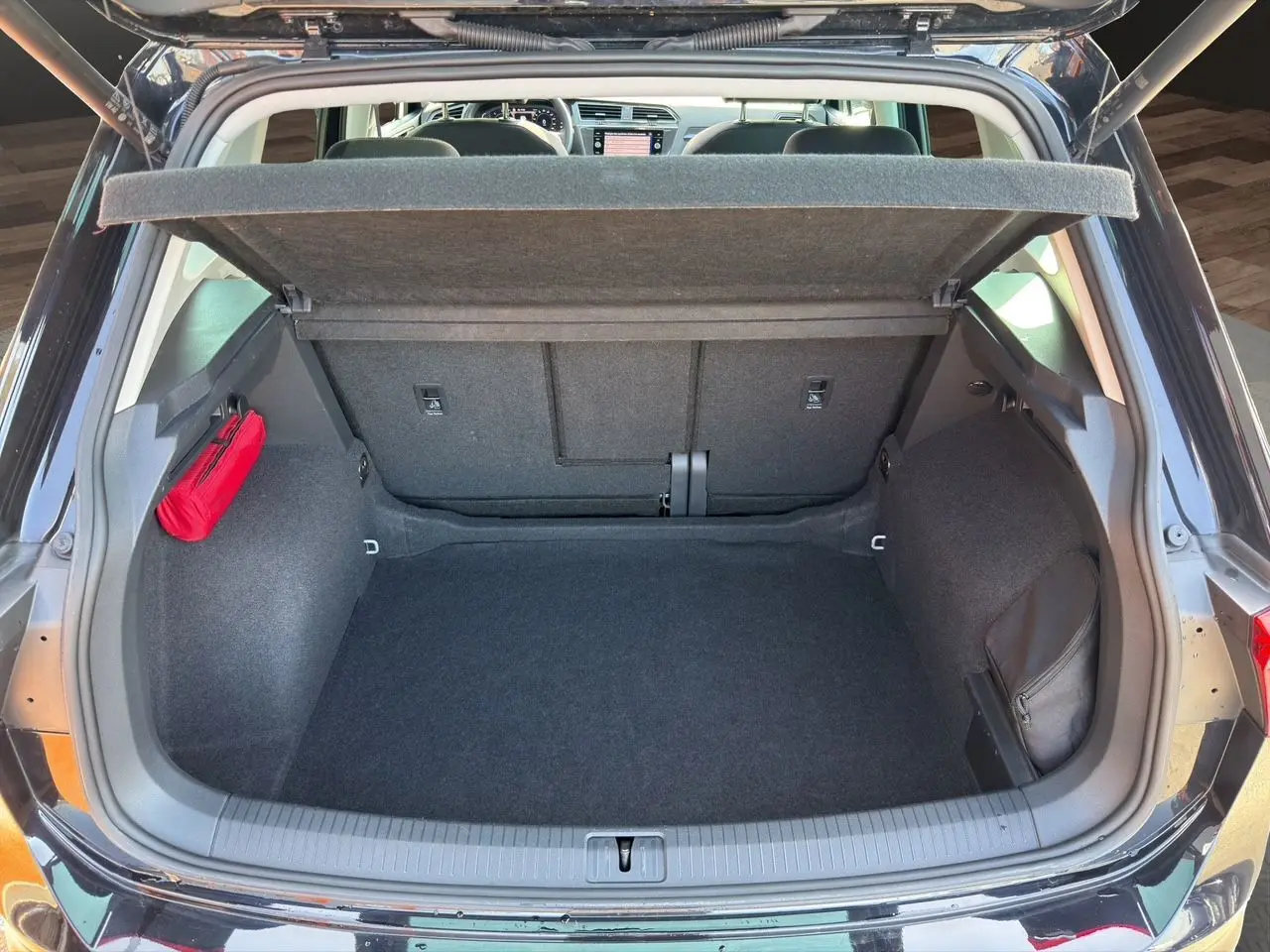 Coffre ouvert vu de l'arrière d'un Volkswagen Tiguan noir intense avec tapis noir et rangement latéral rouge.