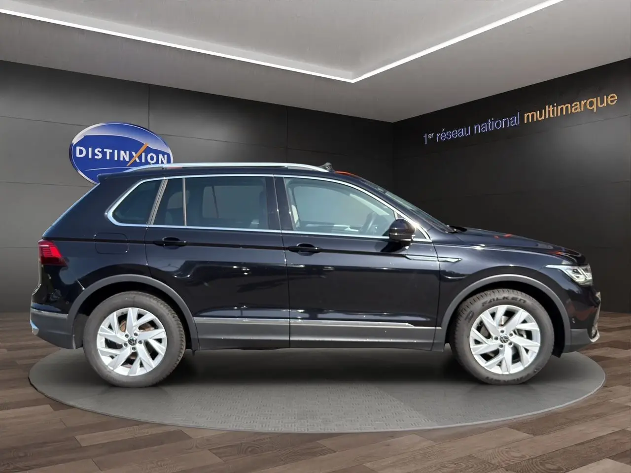 Profil côté gauche du Volkswagen Tiguan noir intense 2022 avec jantes alu 18 pouces dans un showroom.