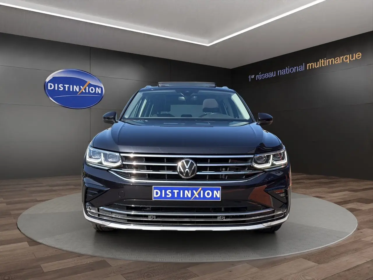 Vue avant du Volkswagen Tiguan noir intense avec calandre chromée et phares LED allumés en showroom.