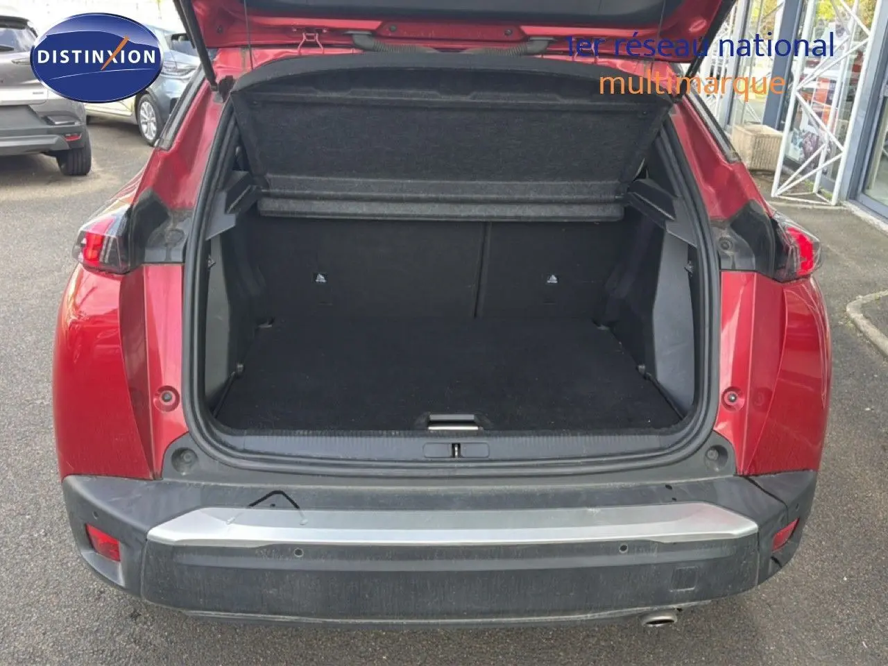 Coffre ouvert vu de l'arrière d'un Peugeot 2008 rouge avec toit noir, montrant l'espace de chargement vide.