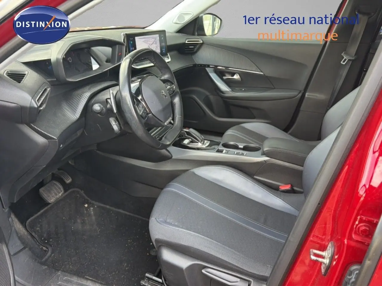 Vue intérieure côté conducteur d'un Peugeot 2008 rouge, montrant le volant, tableau de bord et sièges noirs.