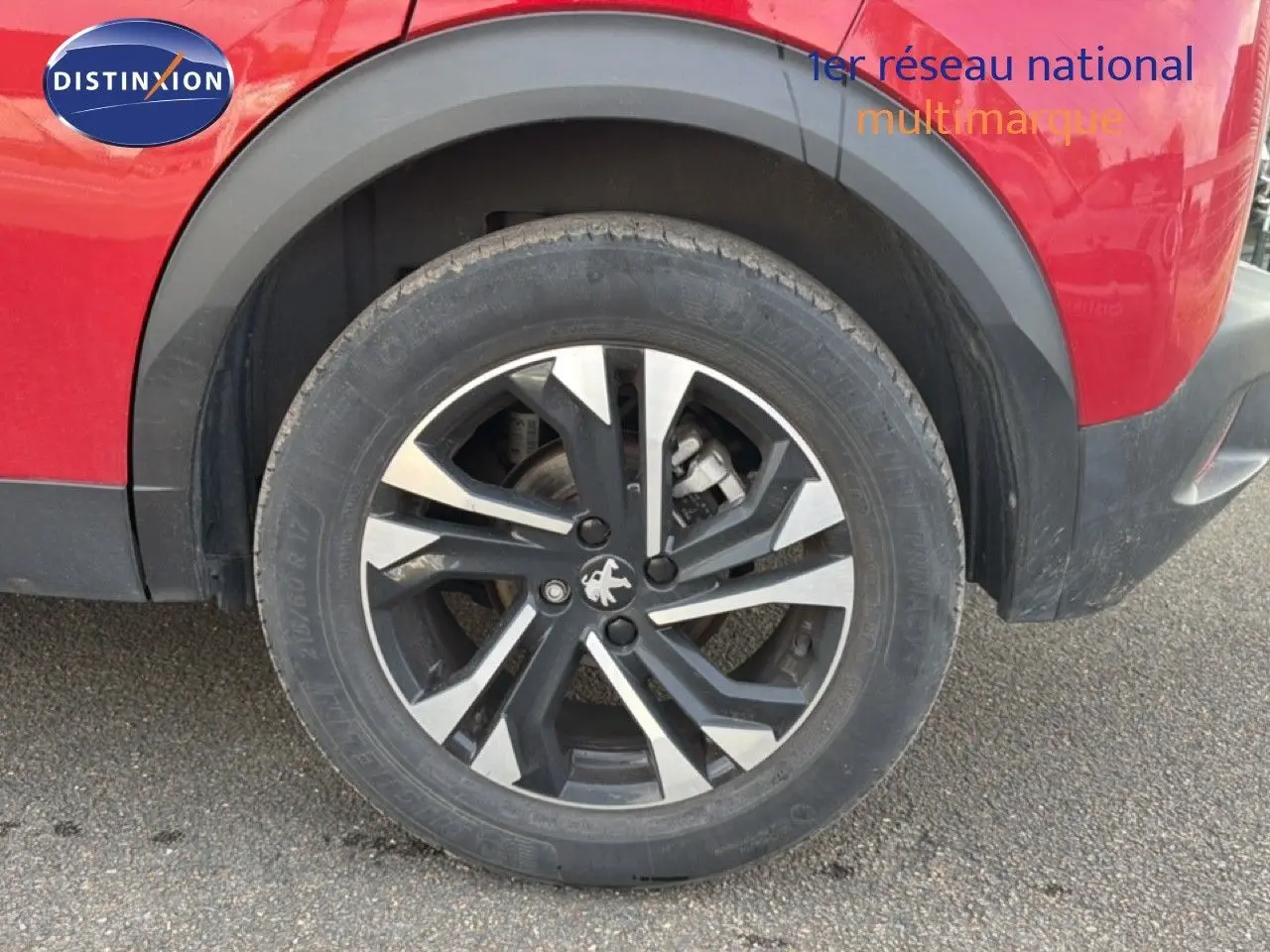 Gros plan sur la roue arrière droite d’un Peugeot 2008 rouge avec jante alliage bicolore et entourage noir.