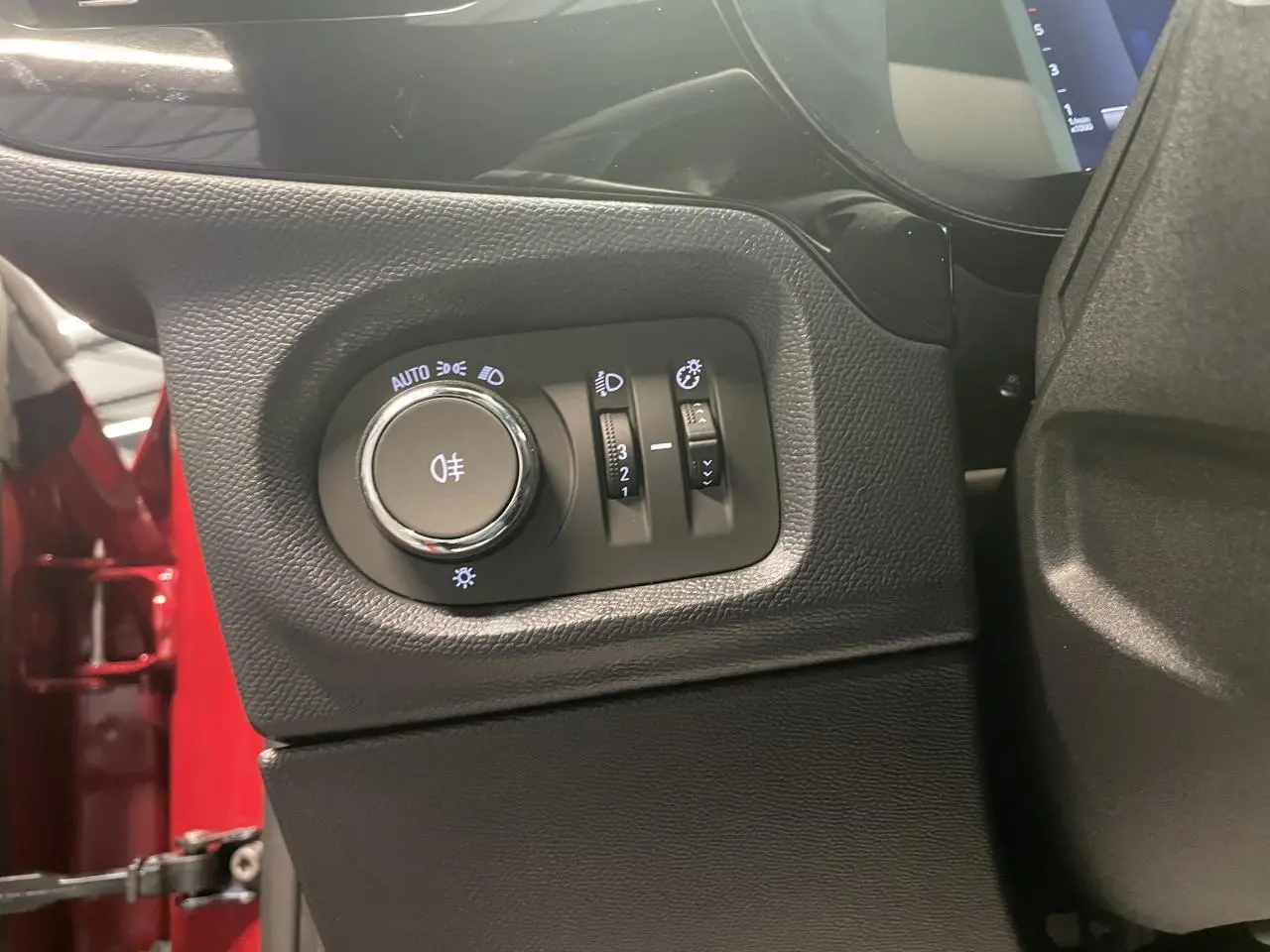 Gros plan sur les commandes d’éclairage à gauche du tableau de bord d’une Opel Corsa rouge, intérieur noir.