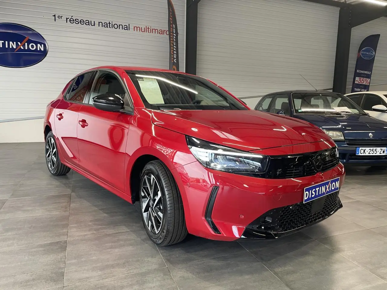 Opel Corsa rouge vue 3/4 avant droit, avec calandre noire et jantes alliage diamantées en showroom.