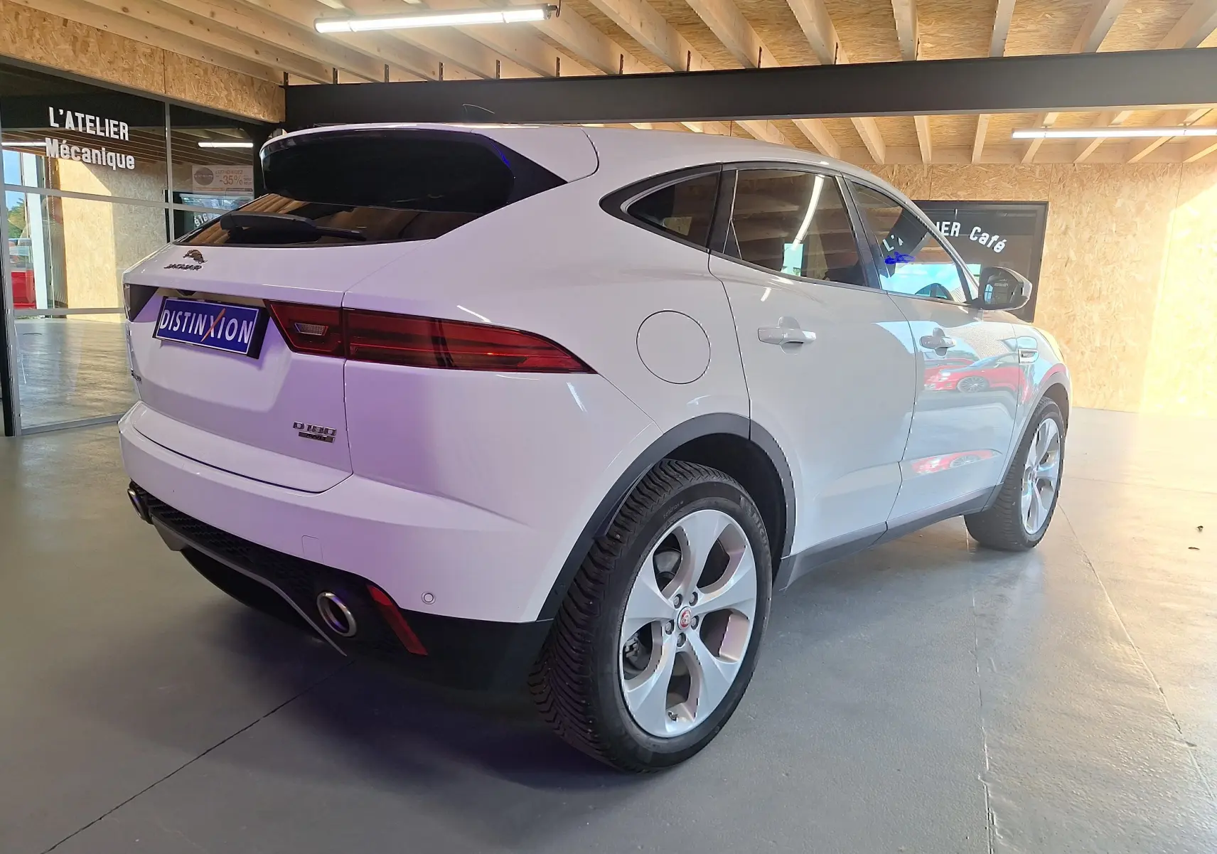 Jaguar E-PACE blanc vue 3/4 arrière droit en intérieur, avec feux arrière LED et jantes alliage visibles.