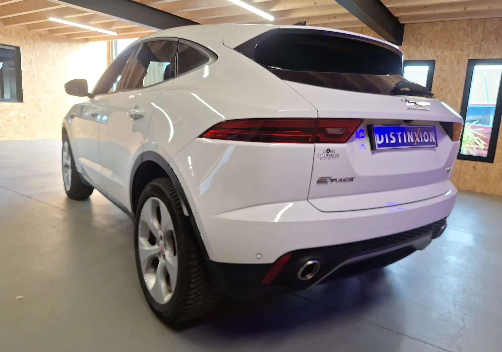 Jaguar E-PACE blanc vue 3/4 arrière droit en intérieur, avec feux arrière LED et sortie d'échappement chromée visible.