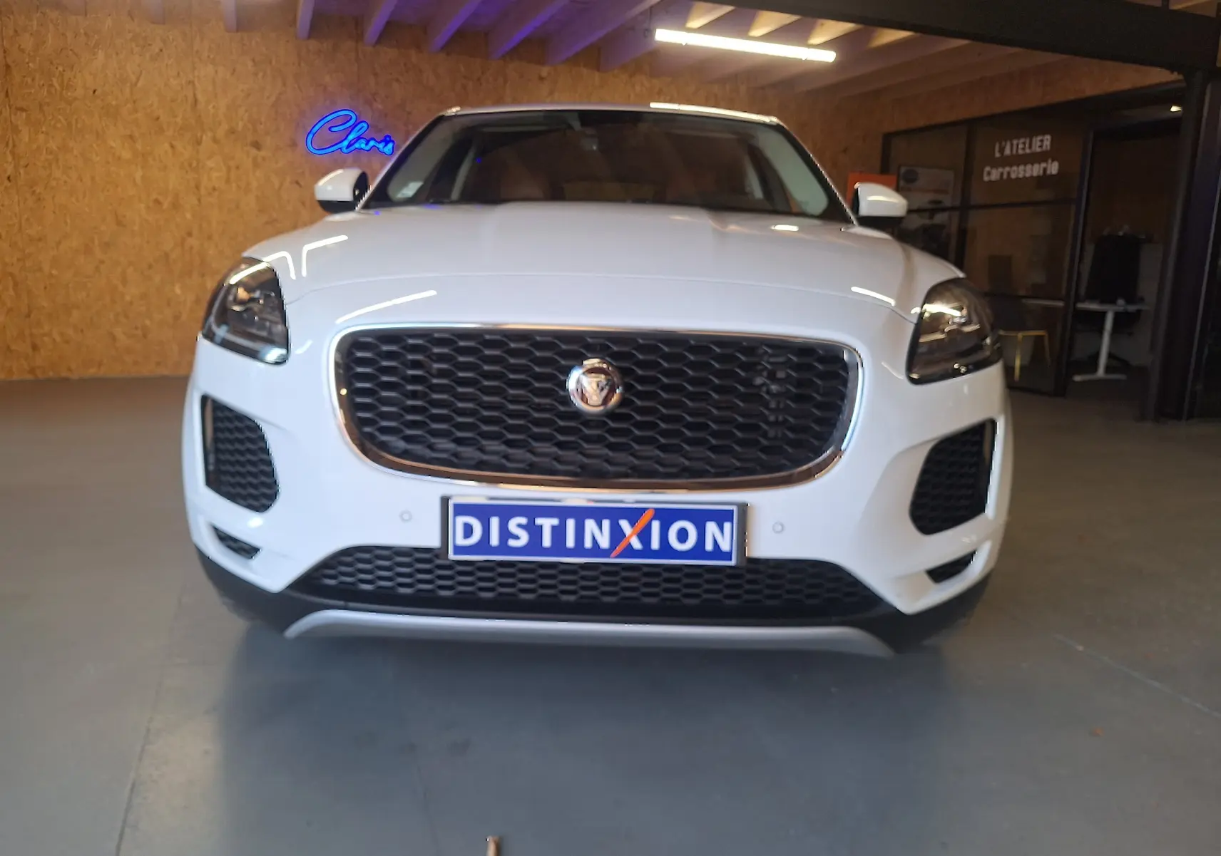 Vue frontale d'un Jaguar E-PACE blanc avec calandre noire et phares LED dans un garage.