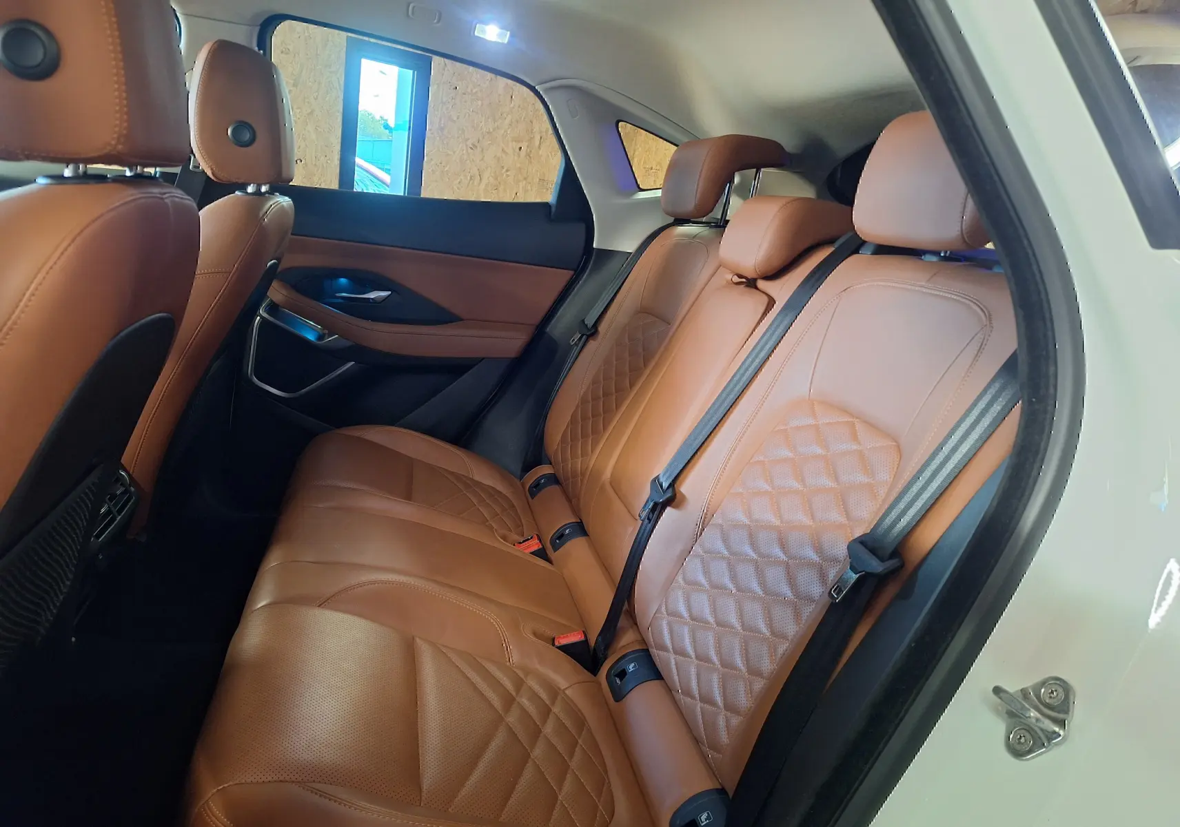 Vue latérale droite sur l'intérieur arrière du Jaguar E-PACE blanc avec sièges en cuir marron matelassé.