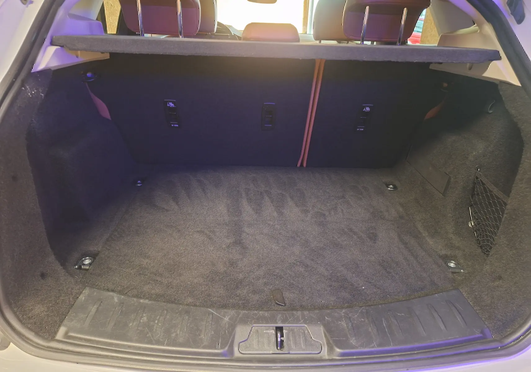Coffre ouvert vu de l'arrière d'un Jaguar E-PACE blanc, espace de chargement avec tapis noir et filet latéral.